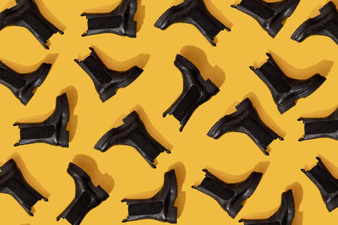 Pattern of black leather boots against yellow background - GEMF04204