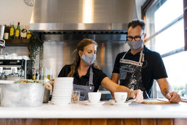 Male and female baristas in protective face mask working at coffee shop during COVID-19 - EGAF00865