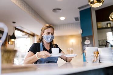 Weibliche Barista serviert Kaffee am Tresen eines Cafés - EGAF00874