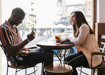 Freund, der seine Freundin mit dem Smartphone fotografiert, während er am Tisch im Café sitzt - EGAF00881