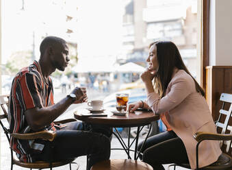 Lächelnde junge Frau im Gespräch mit ihrem Freund, während sie ihre Freizeit in einem Café verbringt - EGAF00882