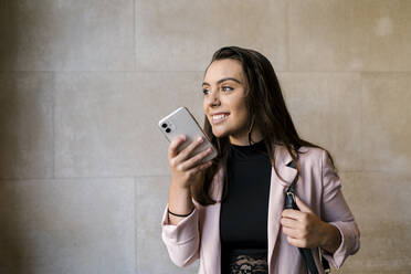 Lächelnde junge Geschäftsfrau, die mit ihrem Smartphone an der Wand eines Cafés spricht - EGAF00893