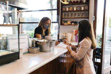 Junge Geschäftsfrau, die während der COVID-19 mit Kreditkarte am Schalter eines Cafés bezahlt - EGAF00899