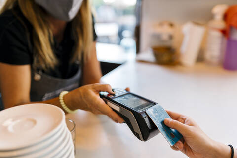 Kassiererin, die von einem Kunden in einem Café während COVID-19 eine Zahlung per Kreditkarte entgegennimmt, lizenzfreies Stockfoto