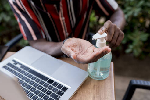 Junger Mann benutzt Händedesinfektionsmittel, während er mit einem Laptop in einem Café sitzt - EGAF00905