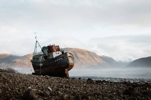 Old rusty fishing boat moored on beach in foggy morning in Scottish Highlands - ADSF16474