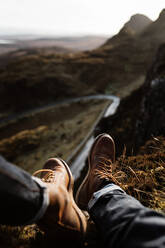 Unbekannter männlicher Tourist in Trekkingstiefeln, der sich auf einem Hügel vor dem Hintergrund der Berge im schottischen Hochland ausruht - ADSF16481