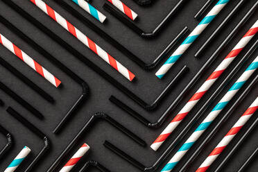 Top view flat lay composition with black and withe and red plastic straws for takeaway drinks arranged in geometric ornament on black background - ADSF16485