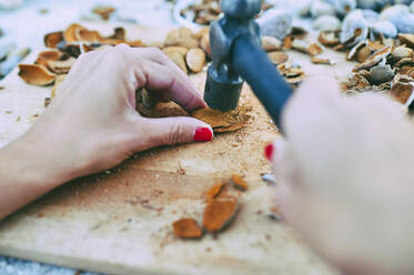 Hands of woman breaking almond husks with hammer - KIJF03340