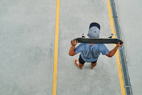 Von oben anonymer männlicher Skater in modischer Kleidung, der mit einem Skateboard auf der Straße steht und wegschaut - ADSF16503