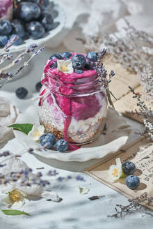 Glasgefäß mit nahrhaftem Joghurt mit gesundem Müsli und frischen Blaubeeren, das morgens zum Frühstück auf dem Tisch steht - ADSF16524