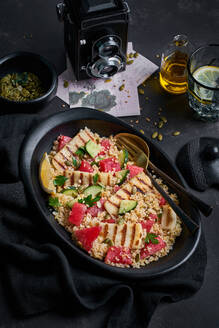 Hochformatiger, köstlicher Bulgursalat mit Halloumi-Käse und reifen Zutaten auf dem Tisch mit Zitronenwasser und Kürbiskernen zum Mittagessen - ADSF16528