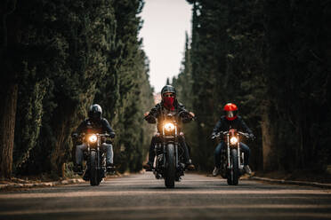 Gruppe von Bikern in schwarzen Lederjacken und Helmen auf leistungsstarken Motorrädern auf einer asphaltierten Straße zwischen grünen Wäldern auf dem Lande - ADSF16562