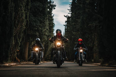 Gruppe von Bikern in schwarzen Lederjacken und Helmen auf leistungsstarken Motorrädern auf einer asphaltierten Straße zwischen grünen Wäldern auf dem Lande - ADSF16563