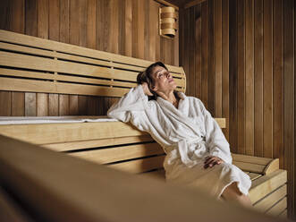Ältere Frau mit Händen hinter dem Kopf entspannt sich in der Sauna im Wellnessbereich - ZEDF03936