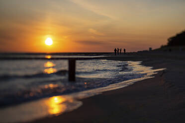 Silhouetten von vier Menschen stehen auf sandigen Küstenstrand bei stimmungsvollen Sonnenaufgang - ASCF01512