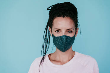 Selbstbewusste Frau mit Schutzmaske im Stehen vor türkisfarbenem Hintergrund - EBBF00794