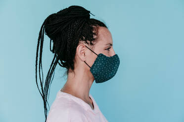 Woman wearing protective face mask with hair bun against turquoise background - EBBF00796