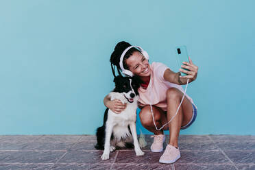 Glückliche Frau nimmt Selfie mit Border Collie Hund gegen türkisfarbene Wand - EBBF00801