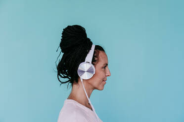 Beautiful woman listening music through headphones against turquoise background - EBBF00806