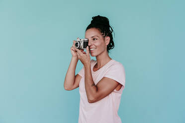 Lächelnde Frau beim Fotografieren mit altmodischer Kamera vor türkisfarbenem Hintergrund - EBBF00812