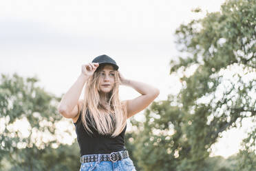 Beautiful young woman wearing cap while looking away against sky - DAMF00526