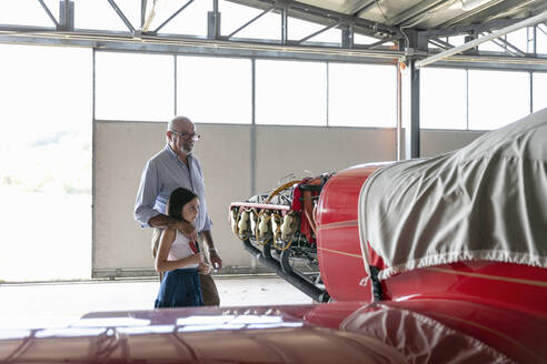 Großvater und Enkelin betrachten ein Flugzeug, während sie im Hangar stehen - EIF00197