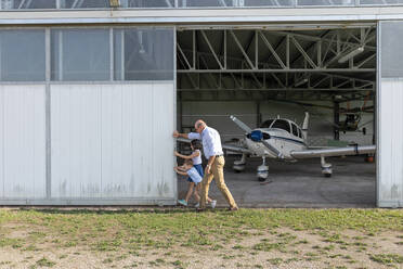 Kinder und Großvater öffnen die Tür eines Flugzeughangars - EIF00198