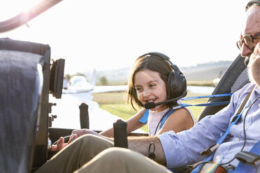 Young little girl inside aircraft cockpit with grandfather at airfield on sunny day - EIF00210