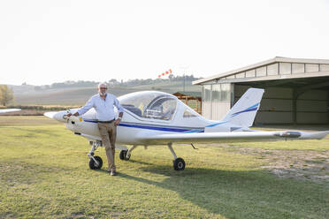 Älterer Mann mit Hand in der Hüfte, der auf einem Flugplatz vor einem Flugzeug steht - EIF00217