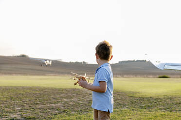 Little boy holding toy airplane while standing at airfield - EIF00225