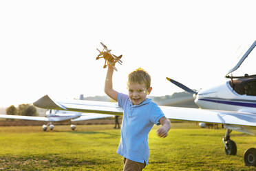 Cute little boy playing with toy plane while standing at airfield - EIF00226