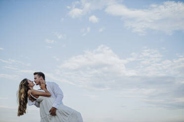 Young couple looking at each other while dancing against clear sky - GMLF00662