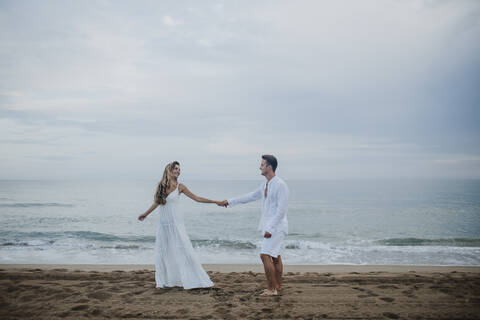 Couple holding hands while dancing against sea at beach stock photo
