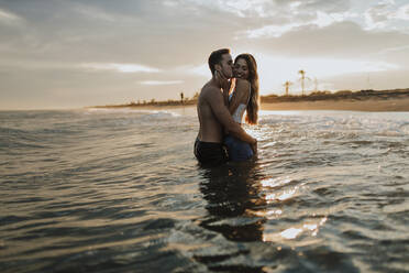 Man kissing woman while standing in water at beach - GMLF00667