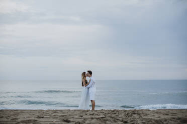 Couple kissing each other while standing against sea at beach - GMLF00668