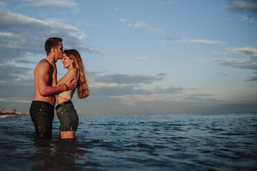 Boyfriend kissing girlfriend while standing in water at beach - GMLF00669