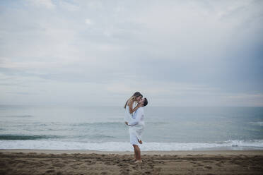 Romantic boyfriend carrying girlfriend while standing on beach - GMLF00670