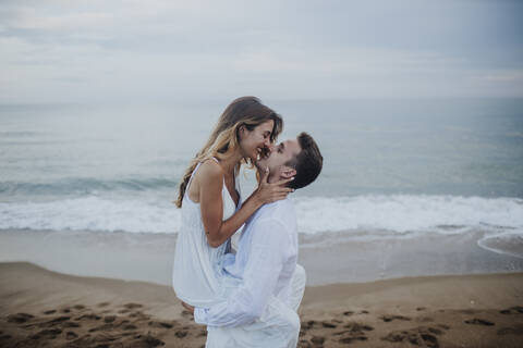 Romantic couple rubbing nose while standing at beach stock photo