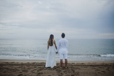 Paar hält sich an den Händen und bewundert die Aussicht auf das Meer am Strand - GMLF00672