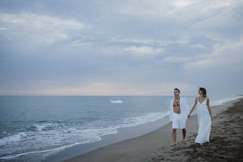 Young couple holding hand while walking on beach during sunset stock photo