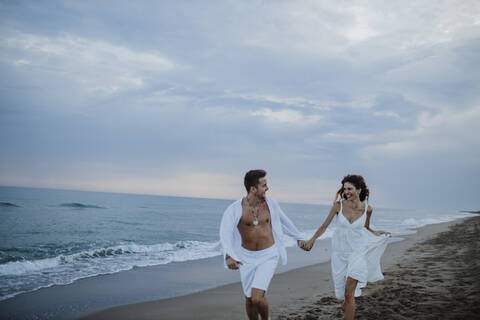 Smiling couple looking at each other while running on beach stock photo