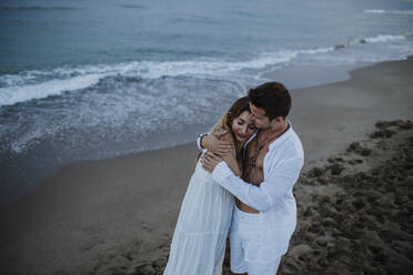 Young man embracing woman while standing at beach - GMLF00687