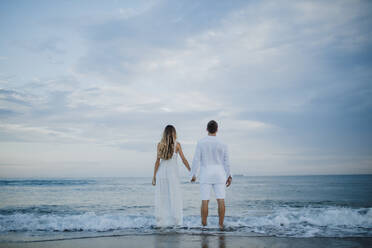 Paar hält sich an der Hand und bewundert die Aussicht am Strand am Rande des Wassers - GMLF00688