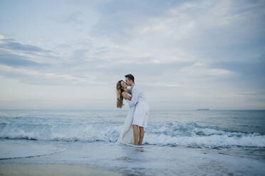 Young man kissing woman while standing in water at beach - GMLF00692