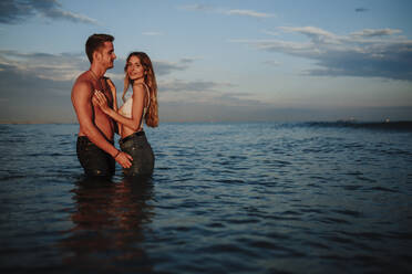 Mann und Frau stehen bei Sonnenuntergang im Wasser - GMLF00703