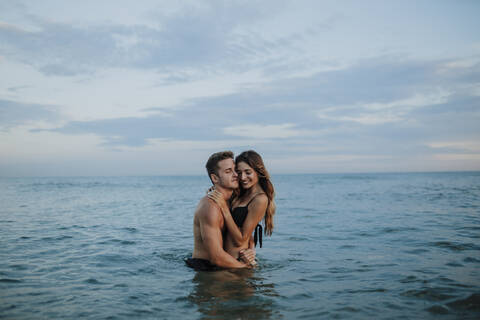 Young man and woman embracing each other while standing at beach stock photo