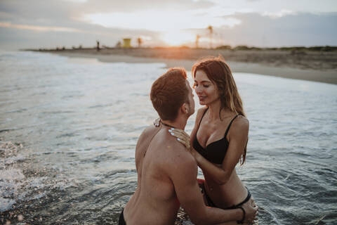 Couple wearing swimwear doing romance in water at beach stock photo