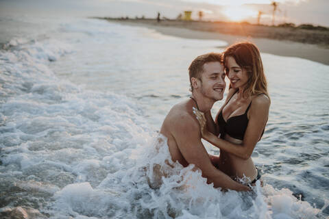 Smiling couple enjoying while sitting in water at beach stock photo