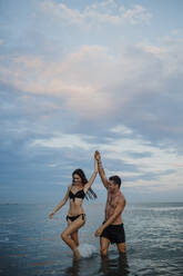 Couple in swimwear walking in water at beach - GMLF00722